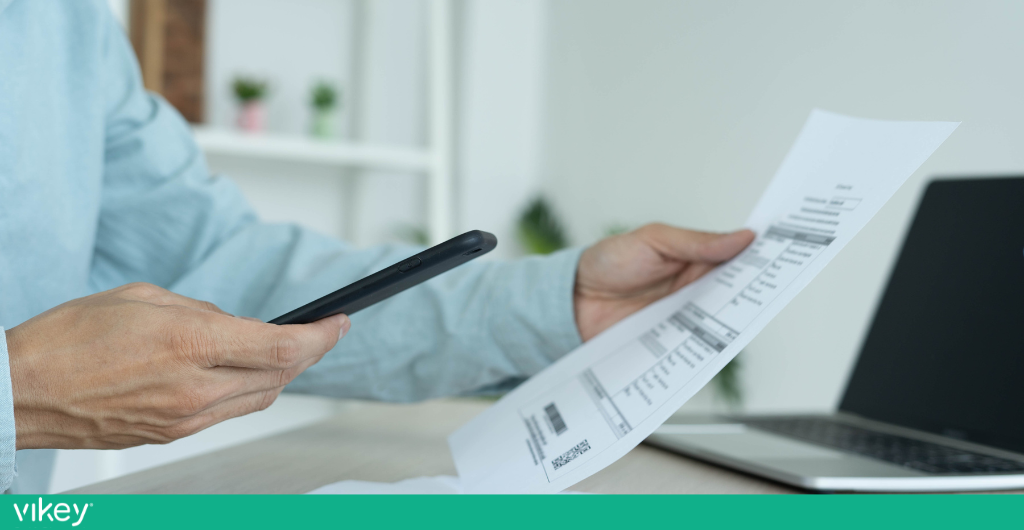 Persona che scansiona una bolletta o un documento fiscale con lo smartphone, seduta davanti al computer.