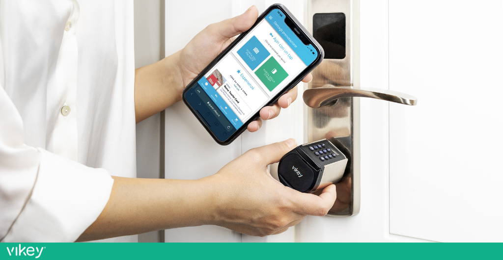 Mani che aprono una porta con serratura elettronica usando uno smartphone con app di accesso digitale.